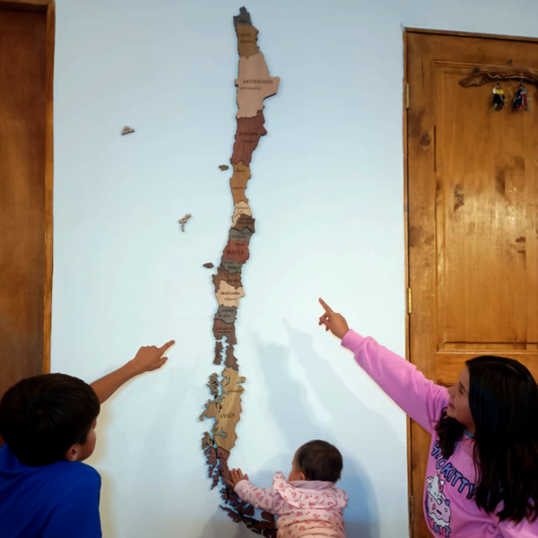 Niños señalando el mapa decorativo de Chile en la pared, con regiones y frontera marcada